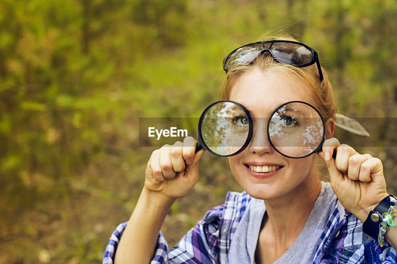 Close-up portrait of young woman holding magnifying glasses in forest