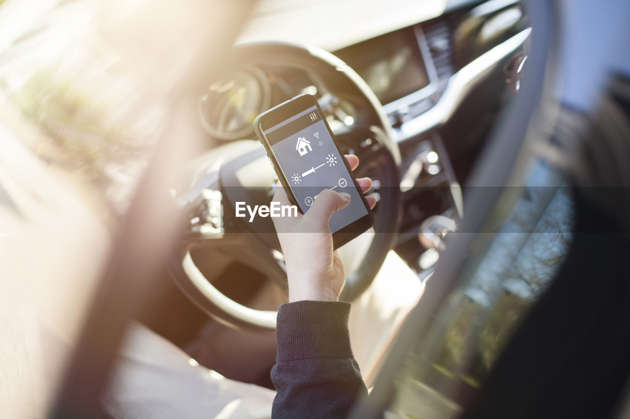 Man in car adjusting devices at home via smartphone