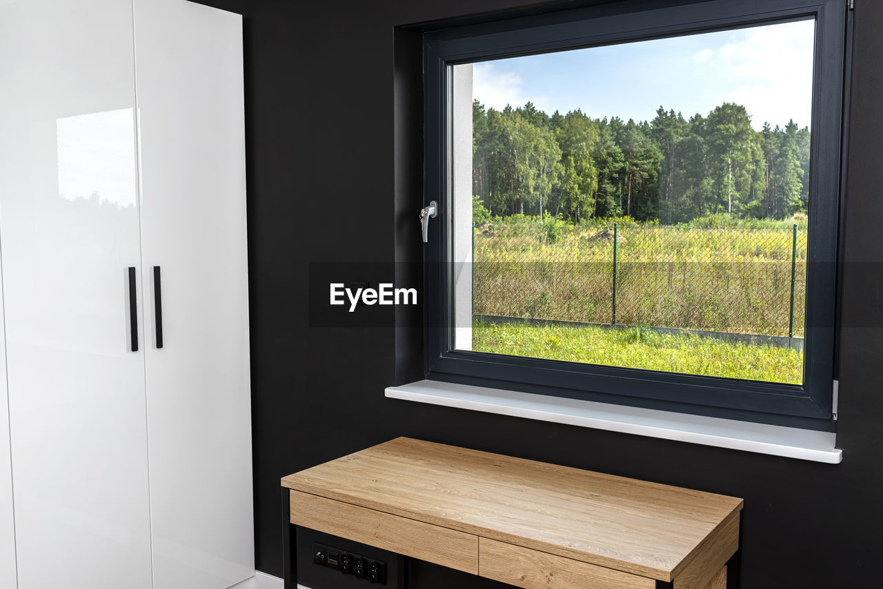 A wooden table under the window in a modern boy room in black and white colors. 