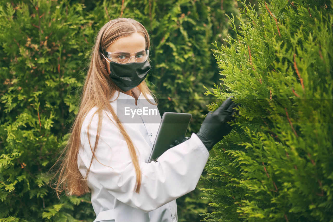 YOUNG WOMAN USING PHONE WHILE STANDING ON PLANT