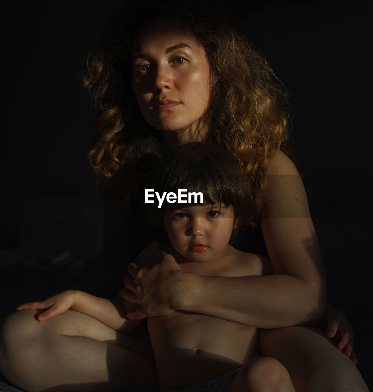 Portrait of woman with baby sitting against black background