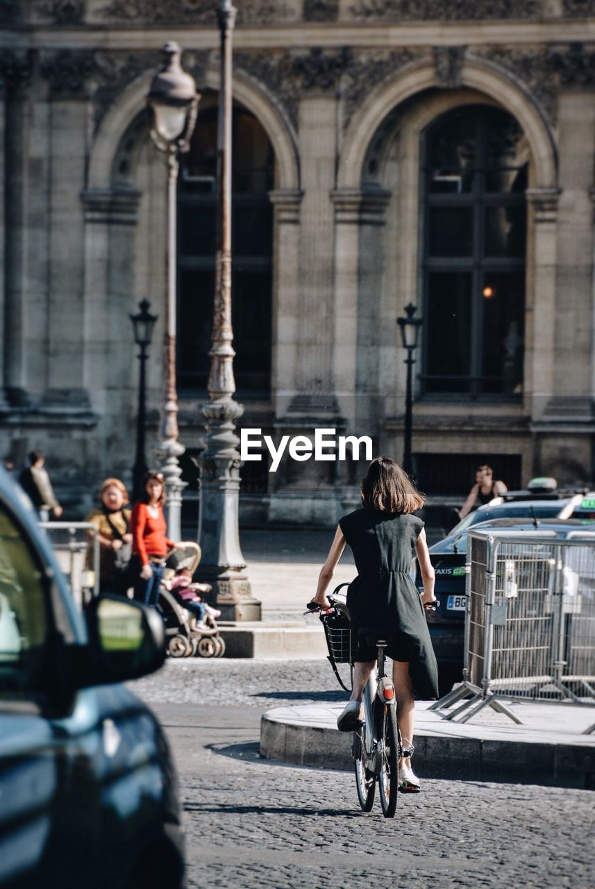 Rear view of woman riding bicycle on street during sunny day