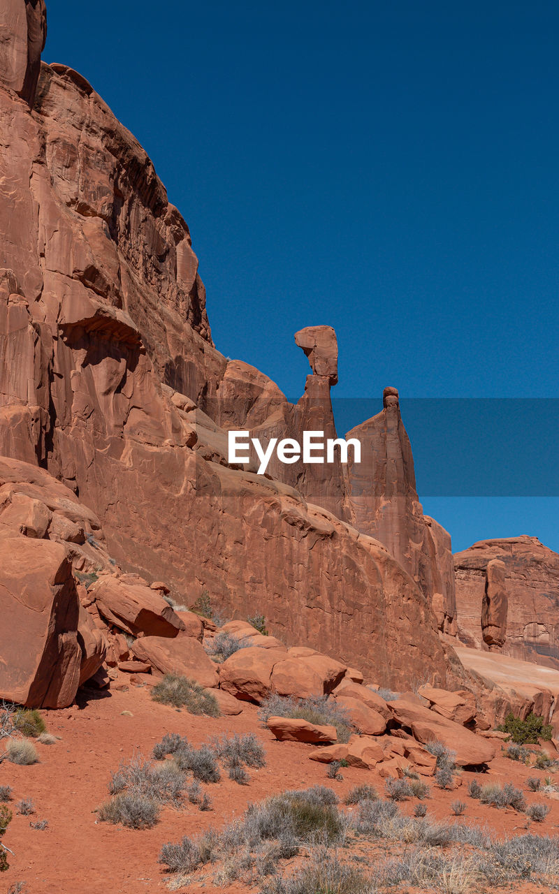 Full frame view of sandstone cliff with rock formations and balancing rock against a clear blue sky