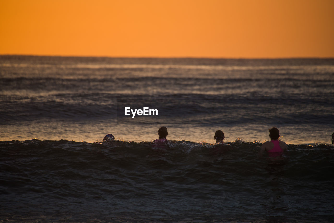 Friends swimming in sea against sky during sunset