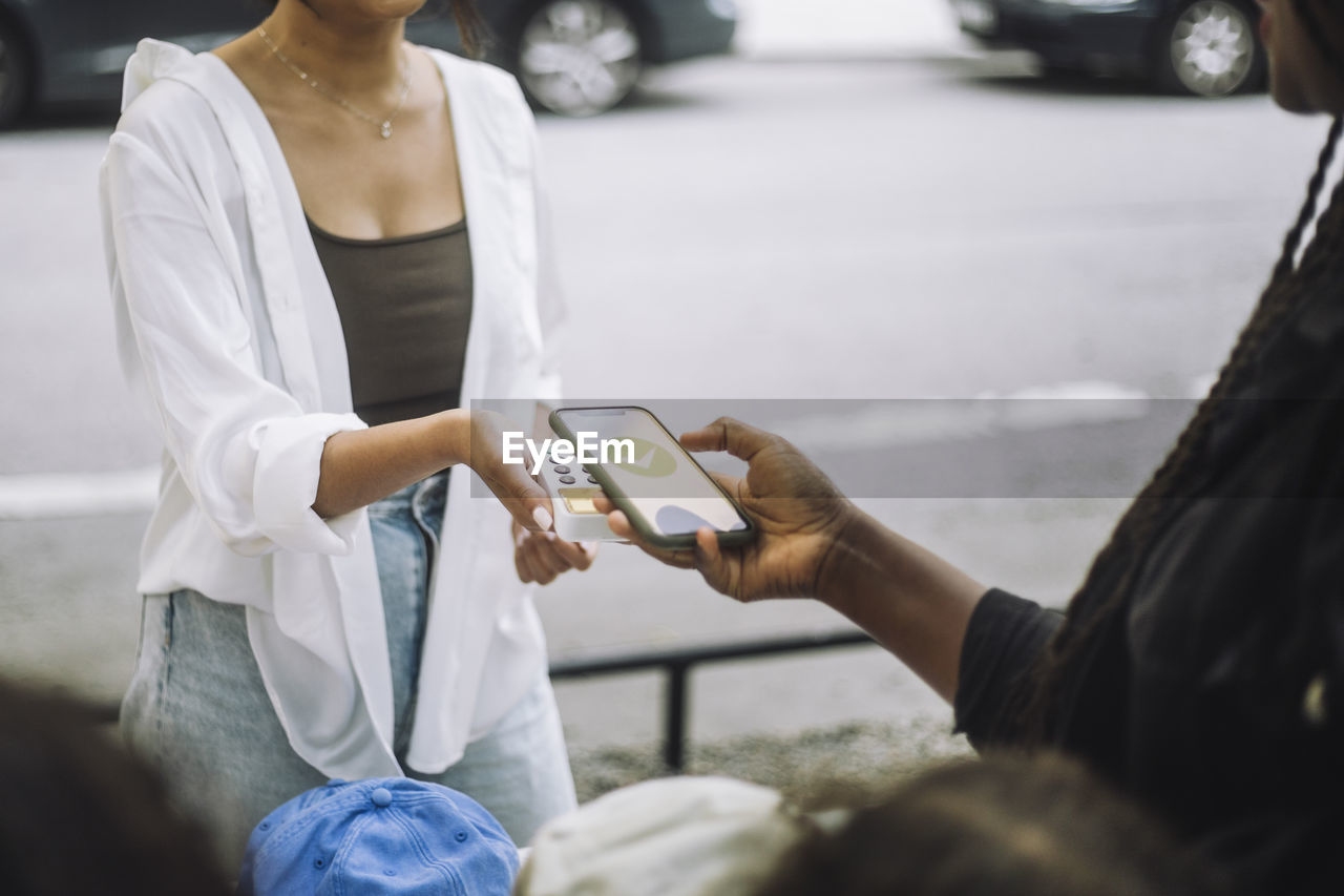 Woman doing online payment through mobile app while shopping at flea market