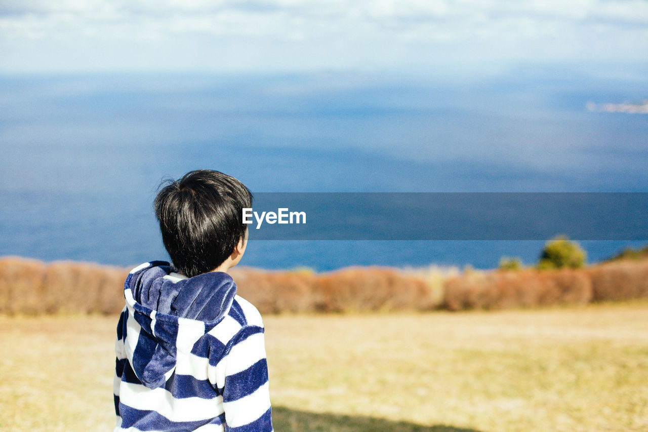 REAR VIEW OF BOY LOOKING AT SEA SHORE