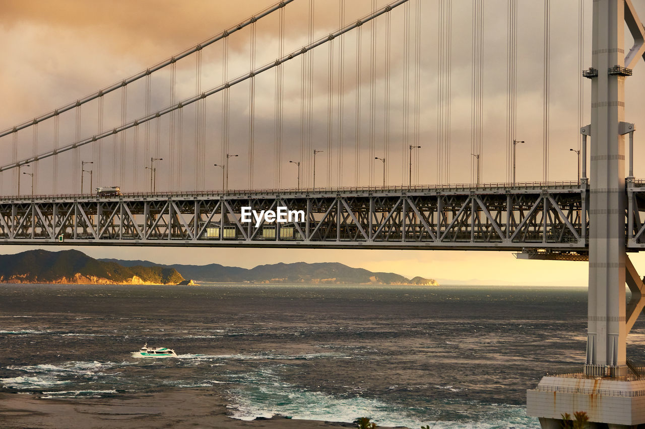 View of suspension bridge over sea against moody sky at sunset