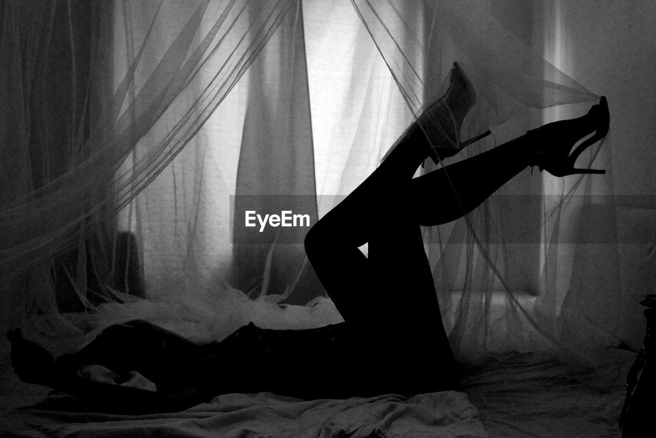 Silhouette woman in high heels lying in bed