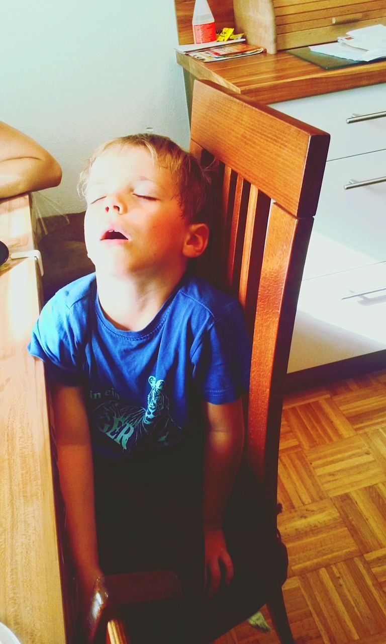 High angle view of boy sleeping while sitting on wooden chair at home