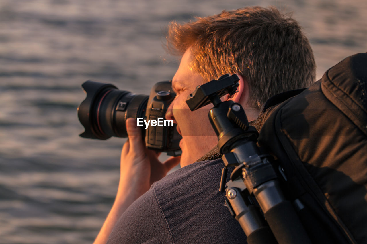 Rear view of man photographing through camera against sea