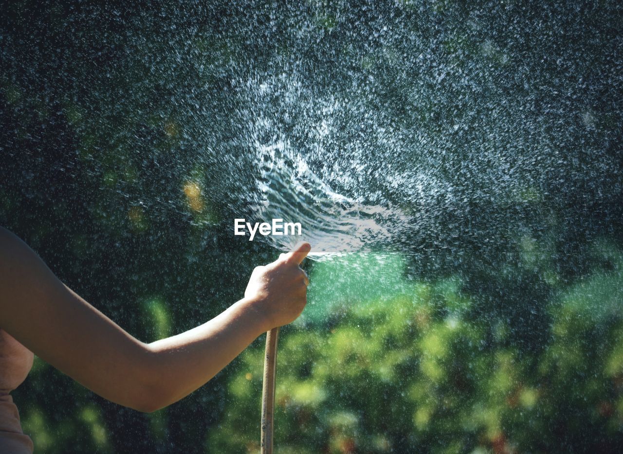 Midsection of woman spraying water with garden hose