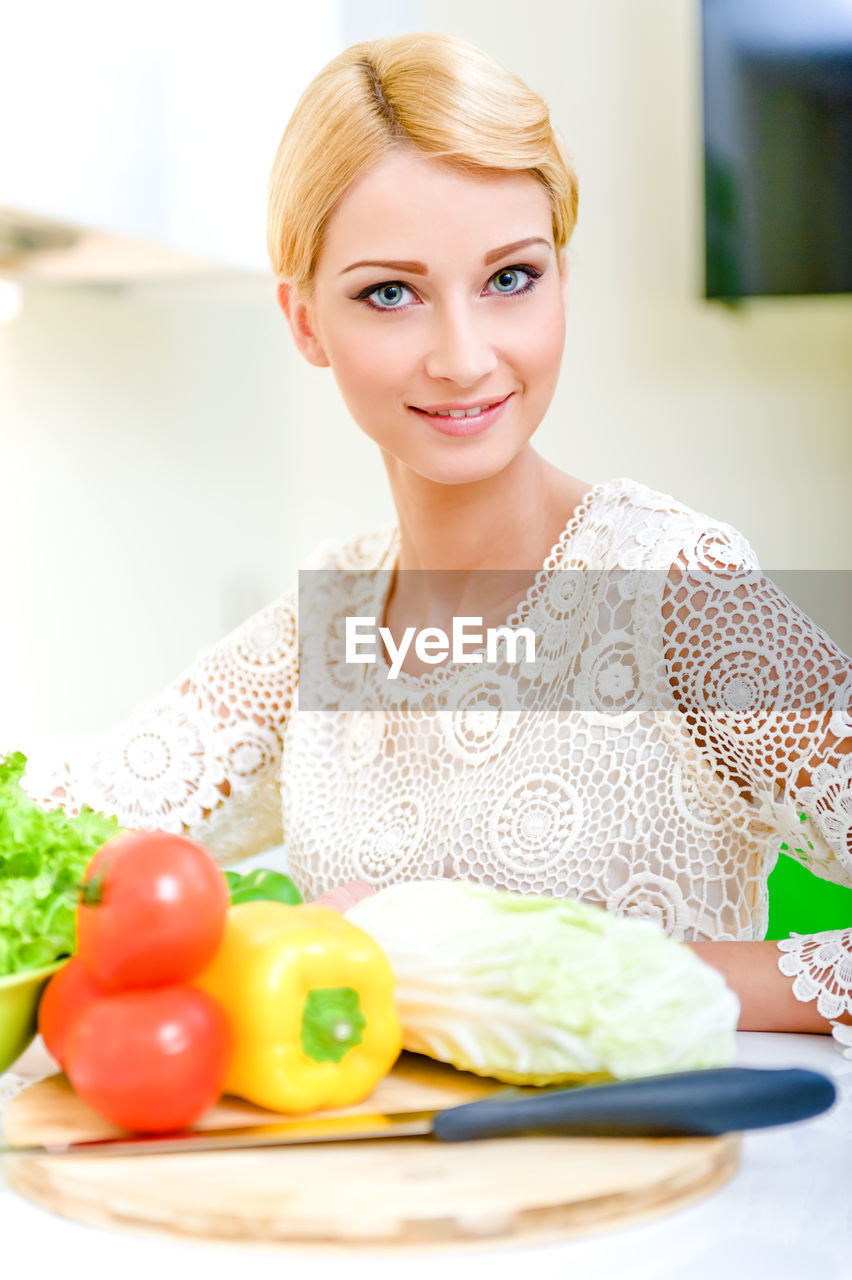 Portrait of young woman with vegetables on table at home