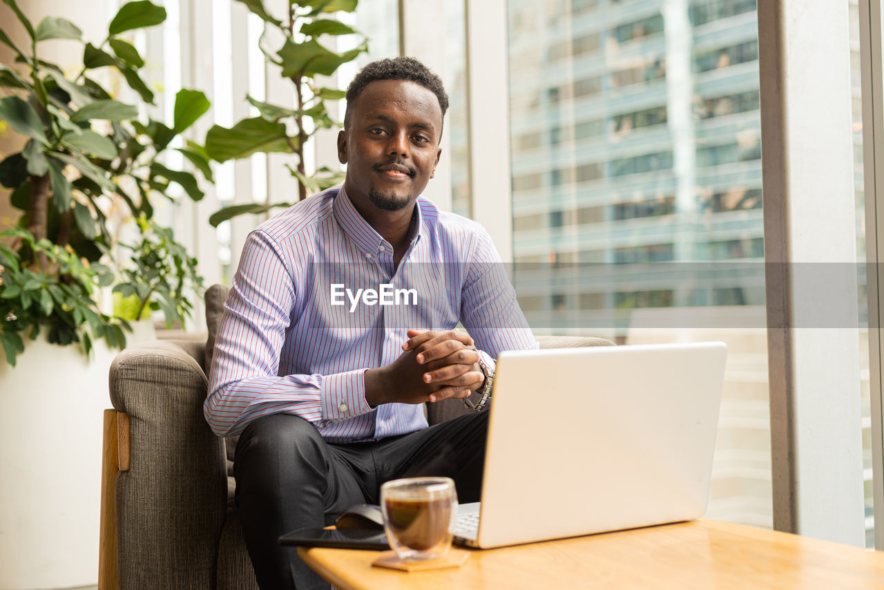 portrait of young man using laptop while sitting on sofa at home