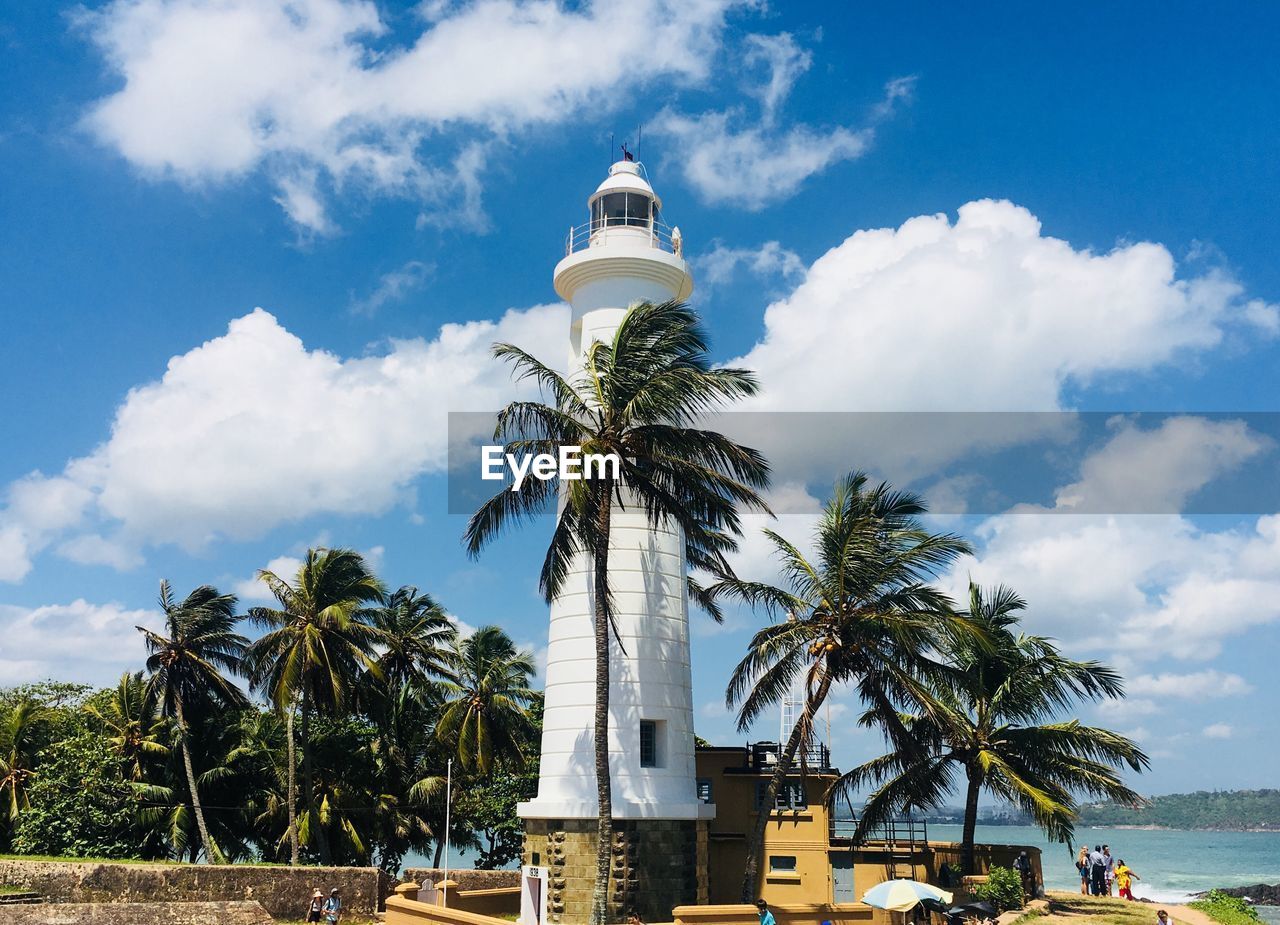 Lighthouse by sea against cloudy sky