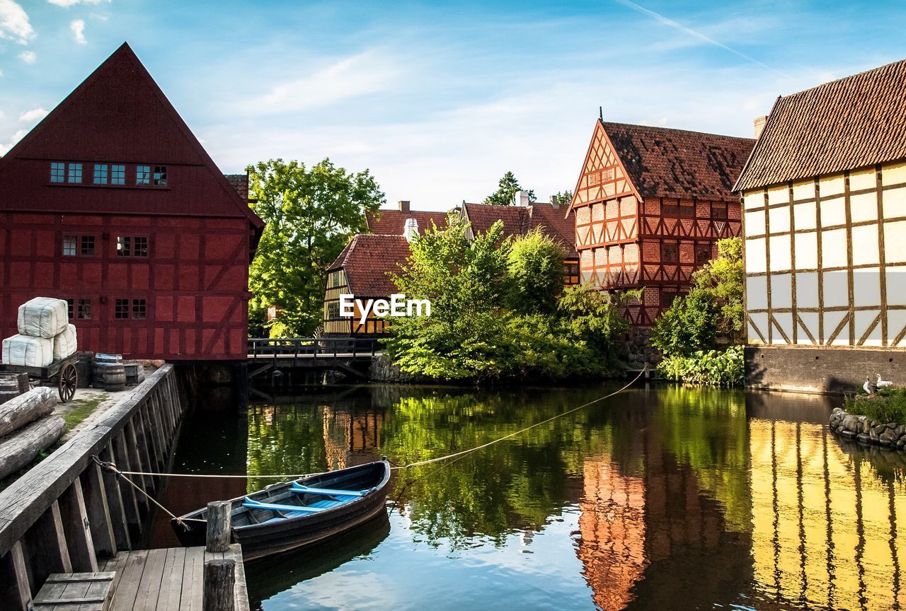 Rowboat moored at canal by old houses in town against sky