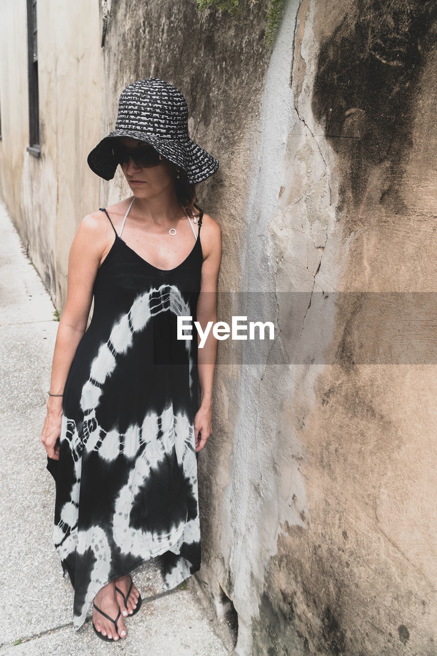 Woman wearing hat and looking away while standing against wall