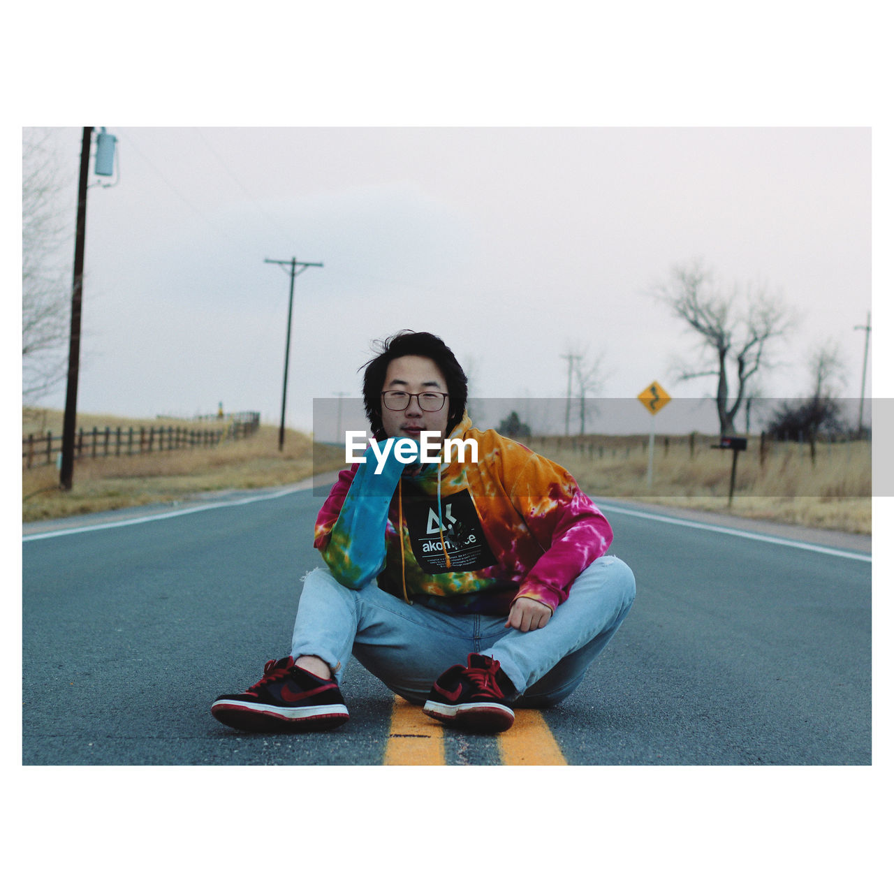 PORTRAIT OF TEENAGE BOY SITTING ON ROAD AGAINST SKY