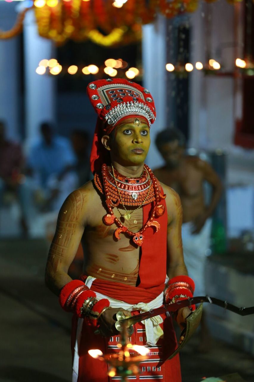 Man in traditional clothing holding weapons during theyyam