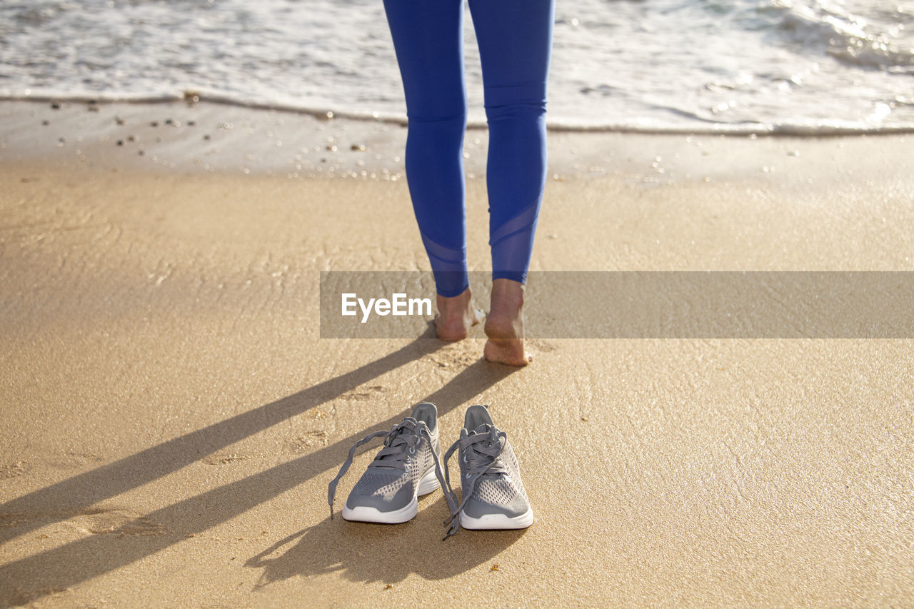 Woman walking barefoot on the beach, shoes in focus, shallow dof