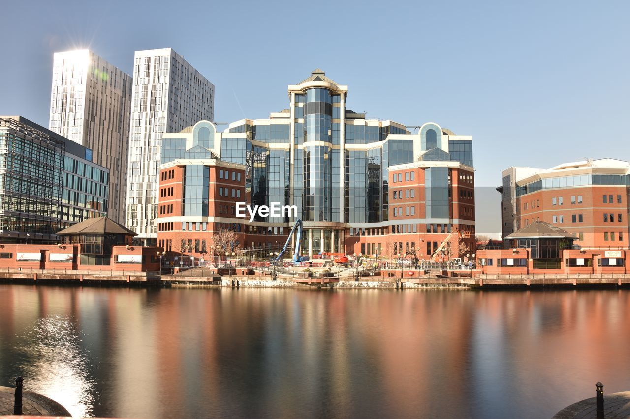 Buildings by river against sky in city