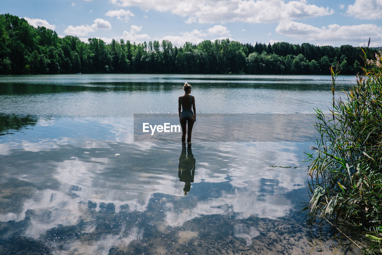 Rear view of woman standing in lake with clouds reflection