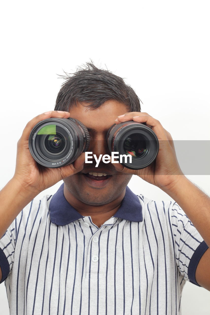 adult, men, camera, one person, holding, technology, portrait, white background, casual clothing, studio shot, young adult, cut out, photographer, lifestyles, occupation, activity, photographing, indoors, arm, lens - eye, person, lens - optical instrument, looking at camera, leisure activity, camera lens, looking