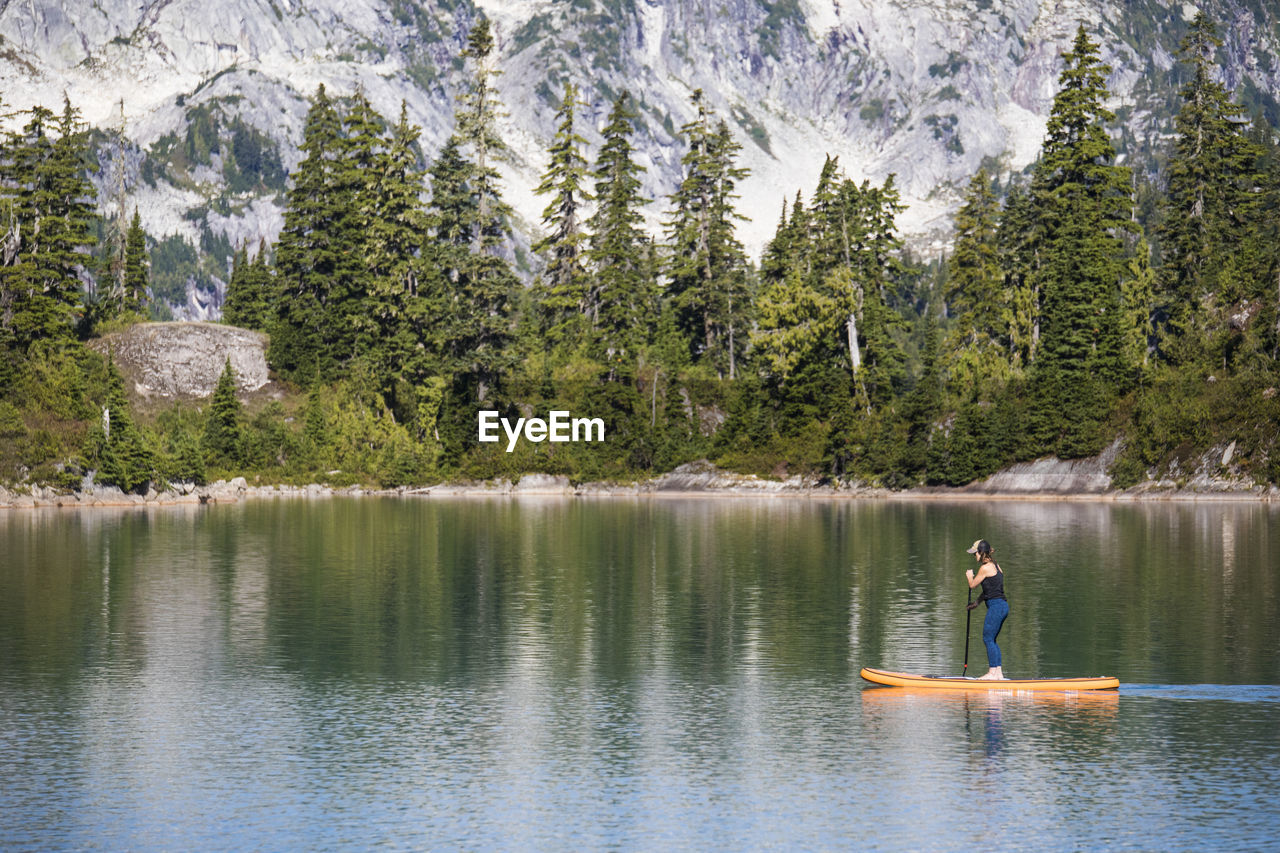 Side view of active woman paddle boarding on mountain lake.