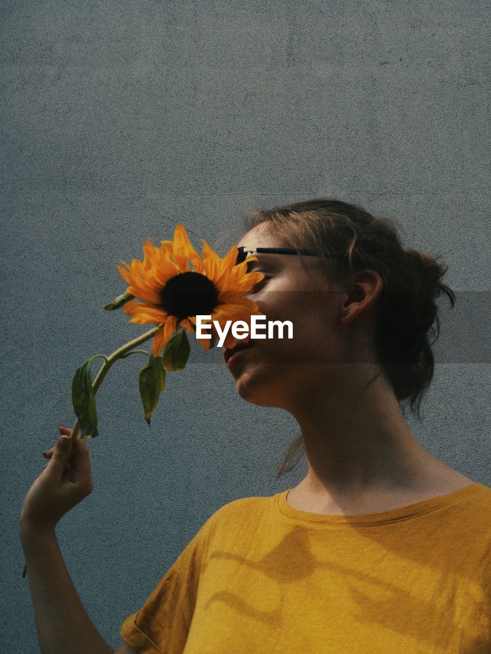 Teenage girl with yellow flower standing against wall