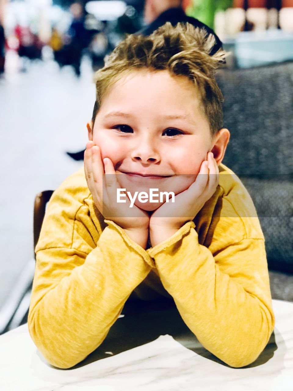 Portrait of smiling boy with hand on chin sitting at sidewalk cafe in city