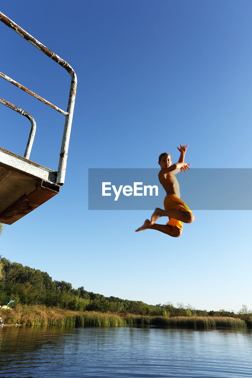 MAN JUMPING IN WATER AGAINST CLEAR BLUE SKY