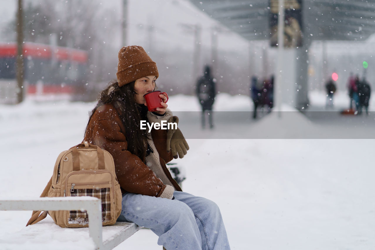 Young traveler girl drink hot tea at train station wait for transport departure for winter vacation