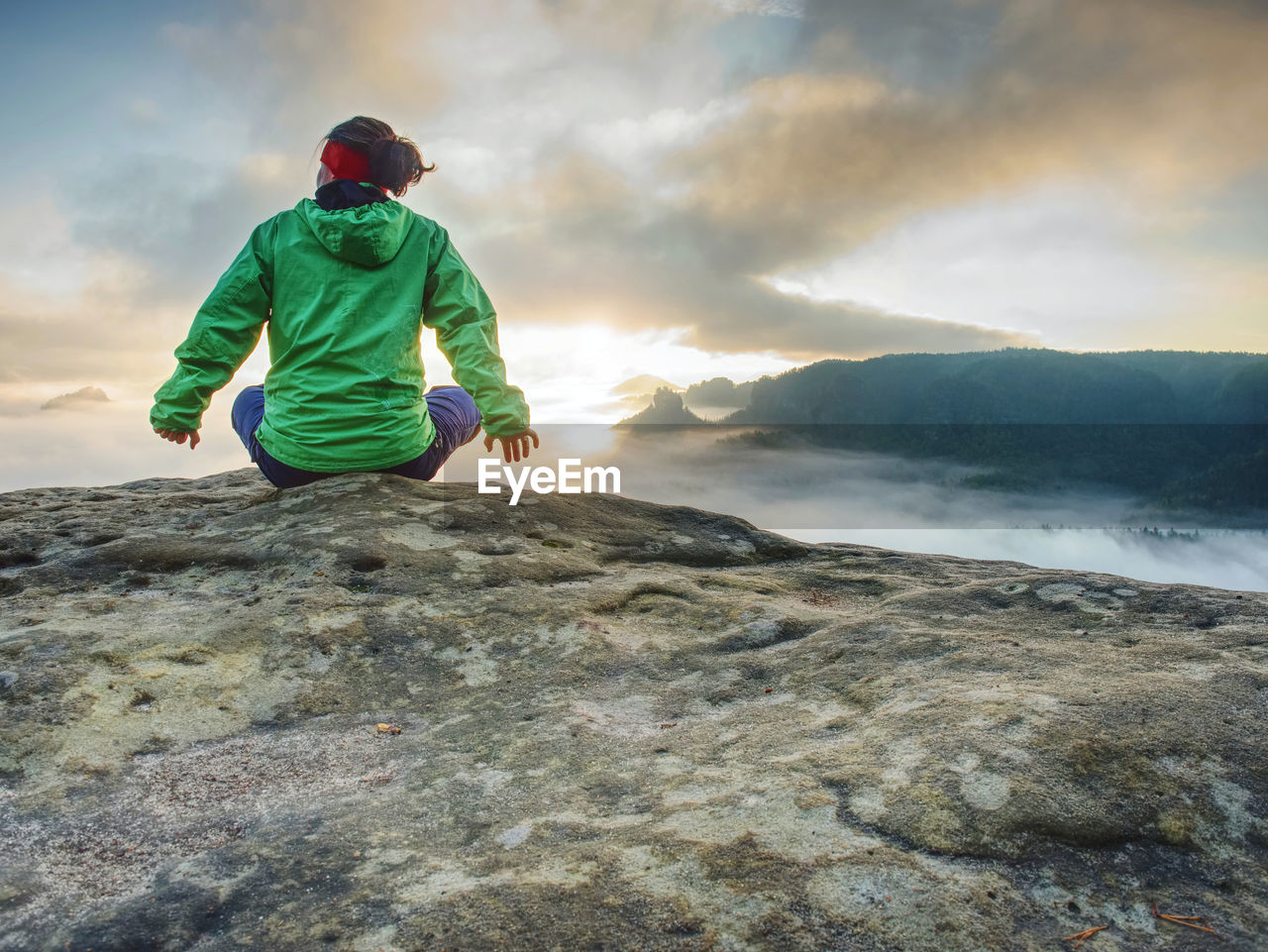 Woman sit on cliff edge and looking to rising sun above misty valley. foggy mountain. man hike