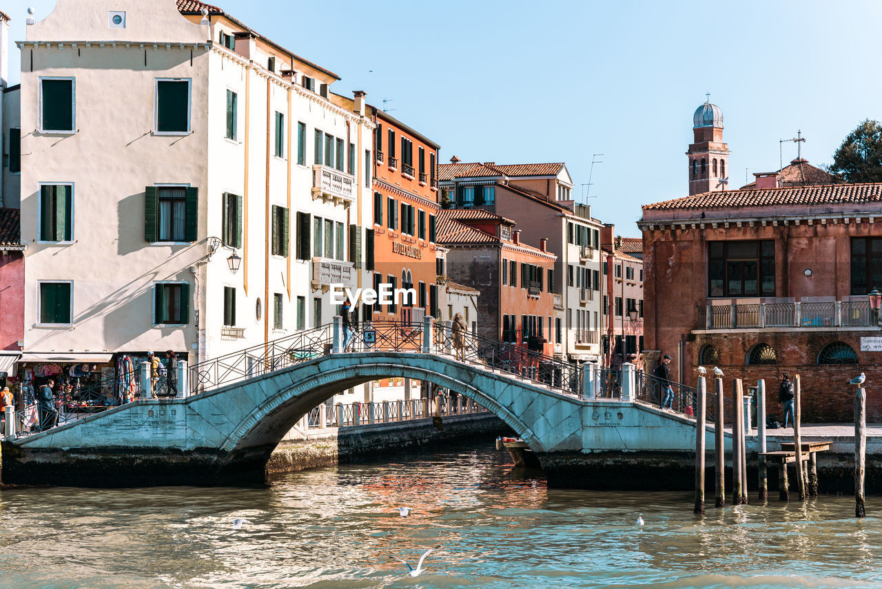 architecture, water, built structure, building exterior, nautical vessel, canal, transportation, gondola, bridge, travel destinations, travel, mode of transportation, boat, tourism, city, waterway, nature, body of water, gondolier, channel, vehicle, town, building, watercraft, trip, sky, vacation, waterfront, holiday, clear sky, tourist, outdoors, reflection, sunny, day, footbridge, sunlight, old, craft, residential district, cityscape, romance, history