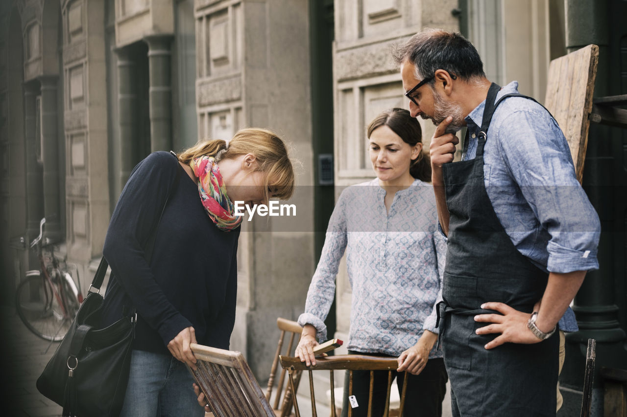 Female costumer choosing chair while retailers standing outside antique shop