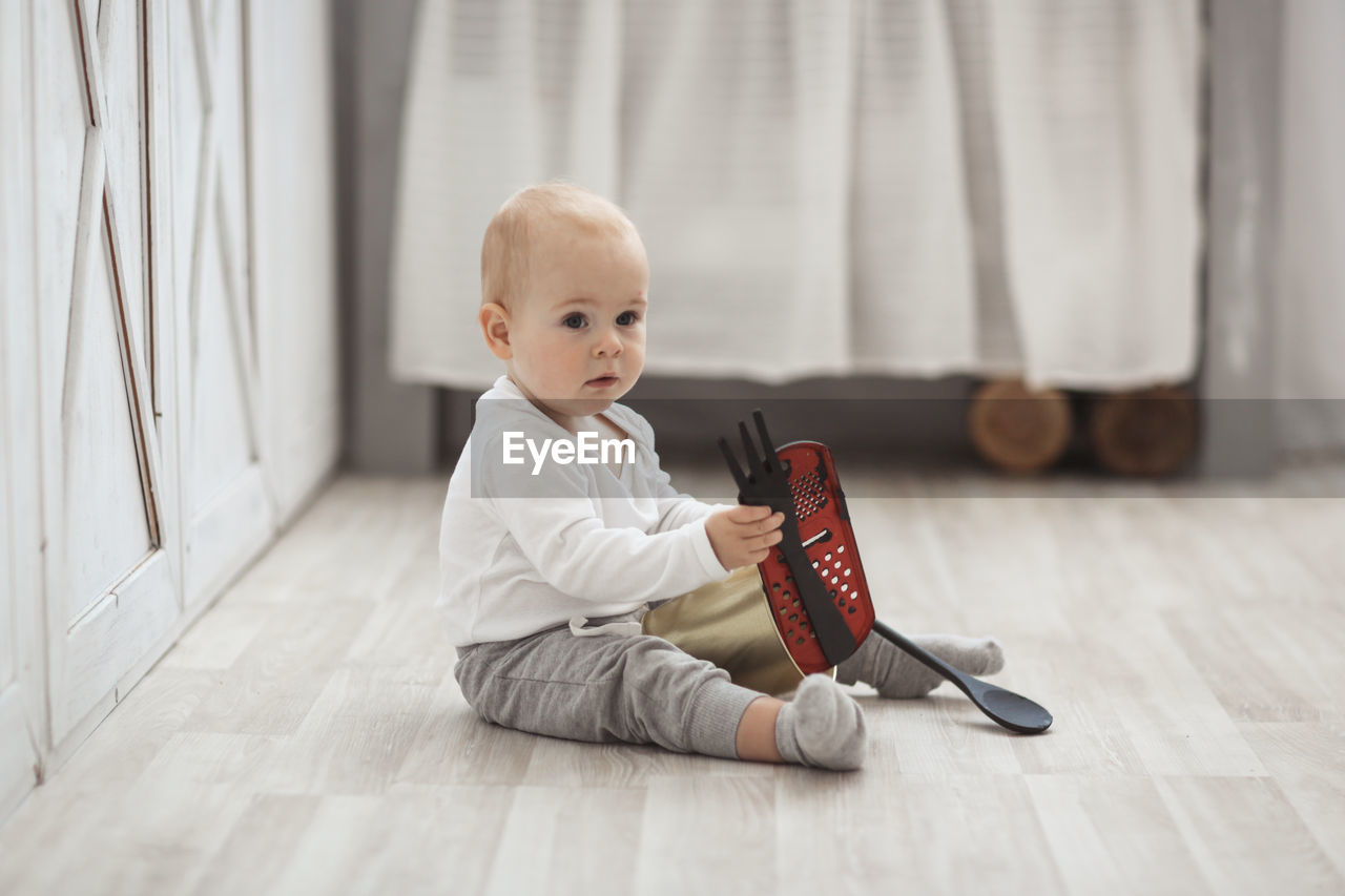 Baby son playing on the floor with kitchen utensils in a real bright interior, lifestyle style.