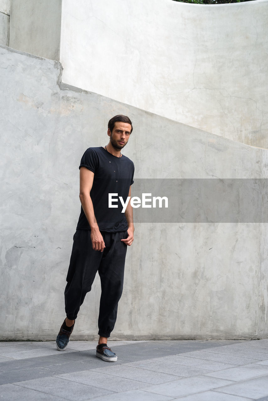 Full length portrait of young man standing against wall