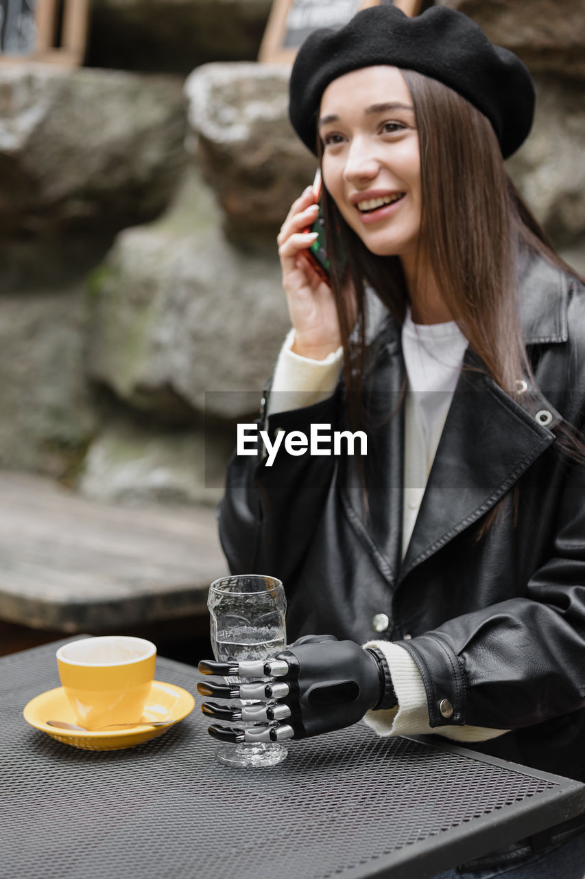 Smiling young woman talking on phone while sitting at cafe