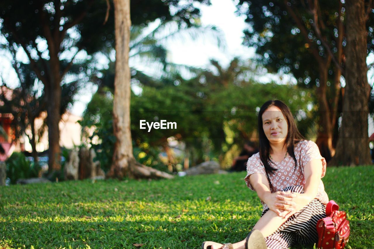 Portrait of smiling woman sitting on field at park