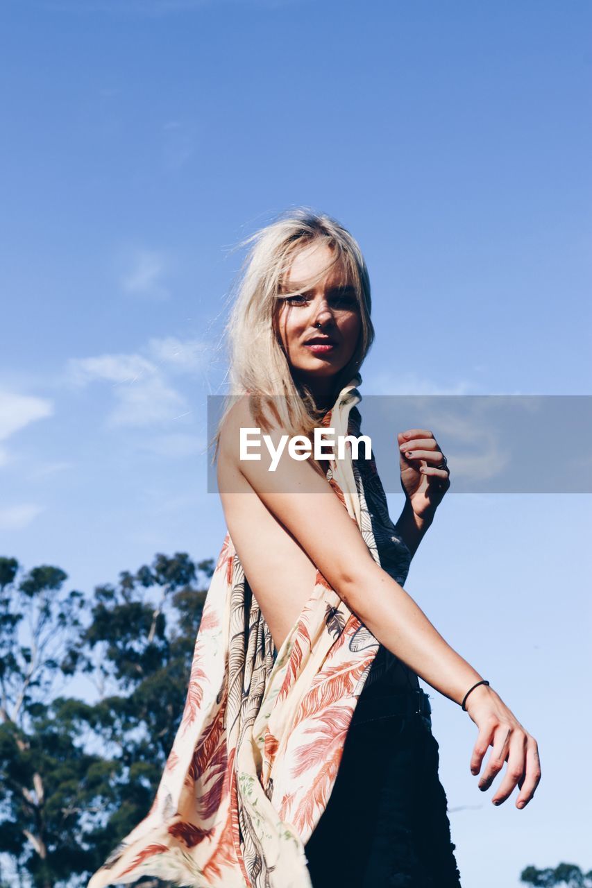 Low angle view of young woman standing against sky