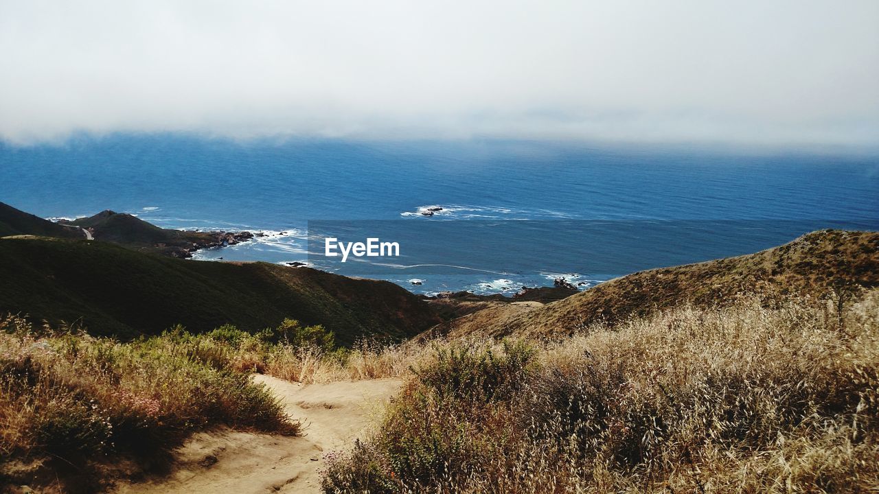 Scenic view of clouds over sea by mountain