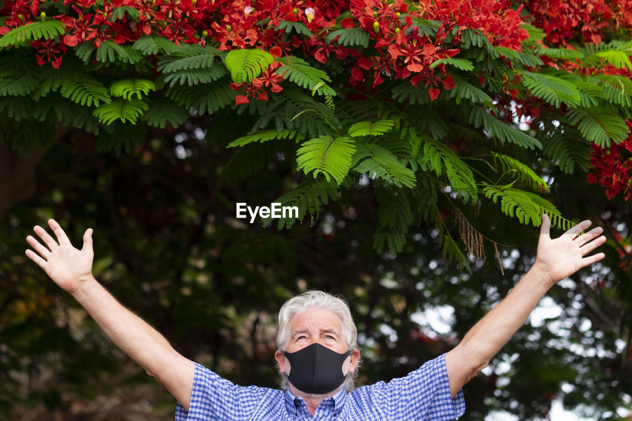 View of senior man with arms outstretched standing by tree outdoors