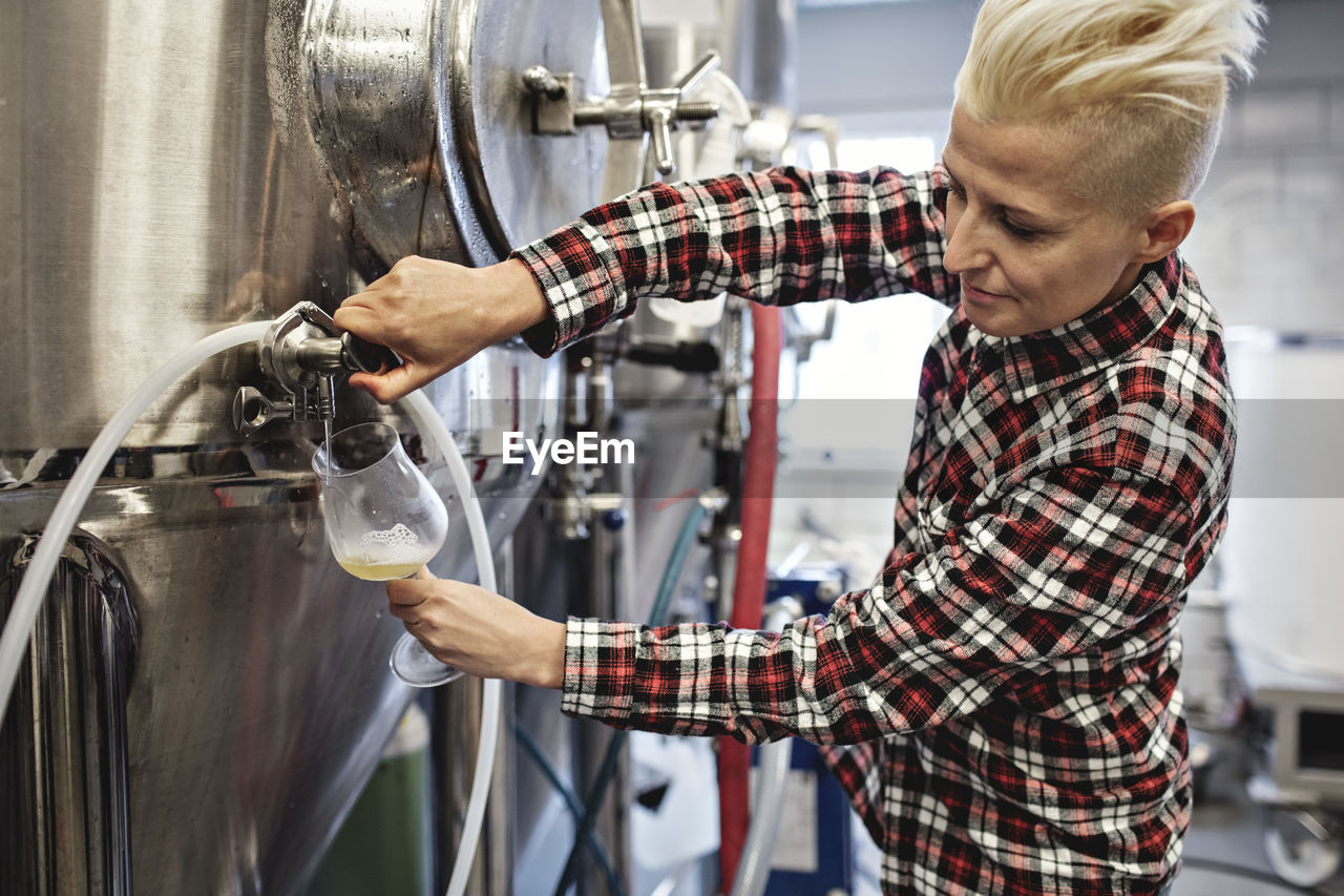 Confident female manager pouring beer from storage tank at factory