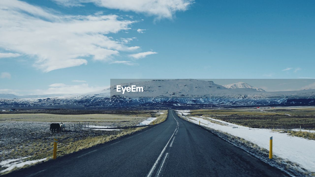 Road by snowcapped mountains against sky