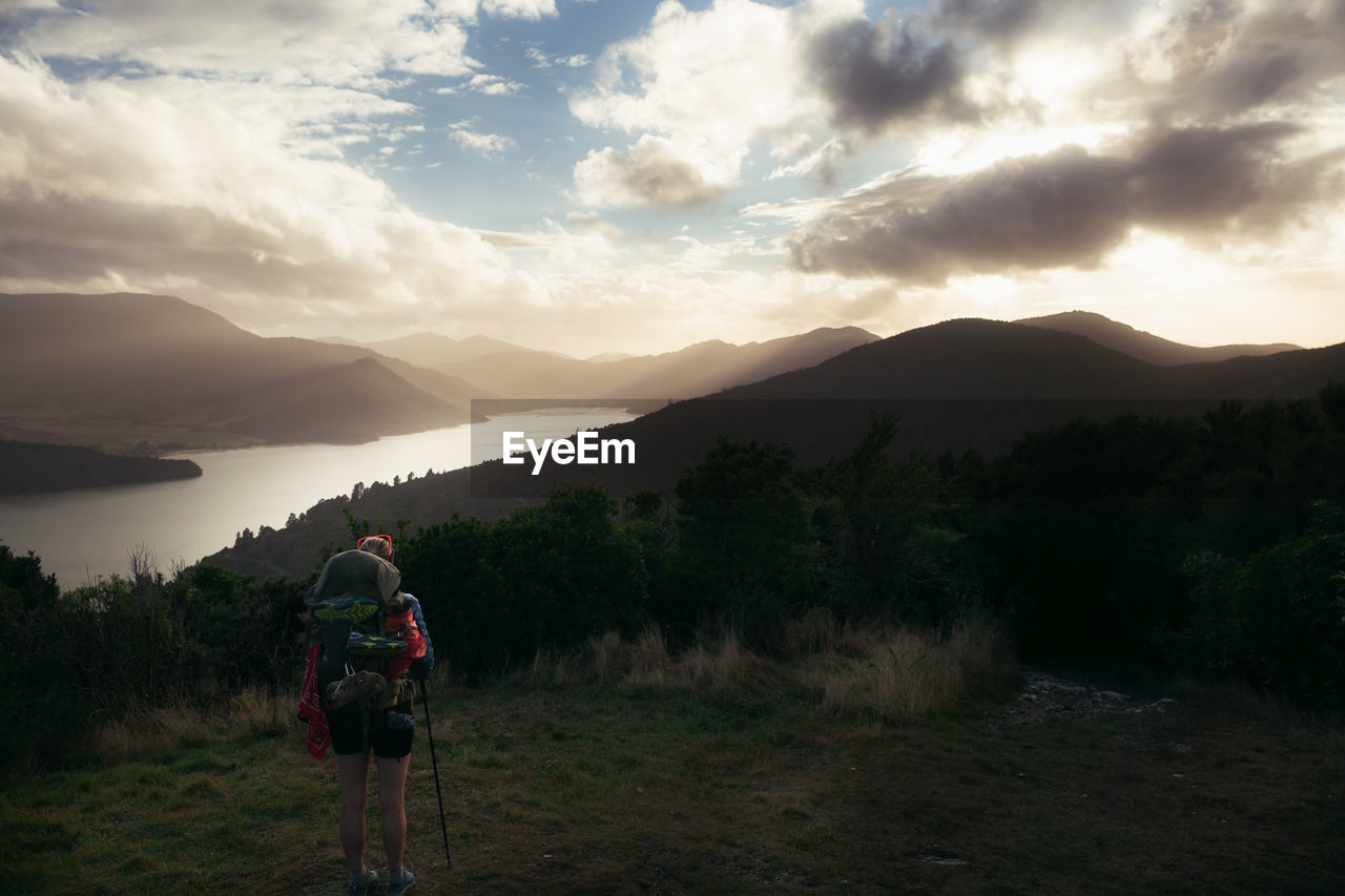 REAR VIEW OF MAN ON MOUNTAIN AGAINST SKY