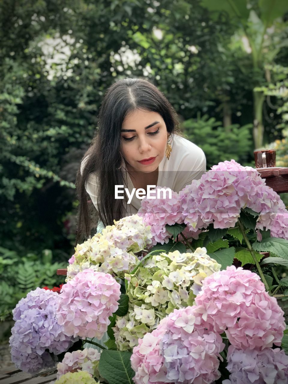 Beautiful young woman with pink flowers against plants