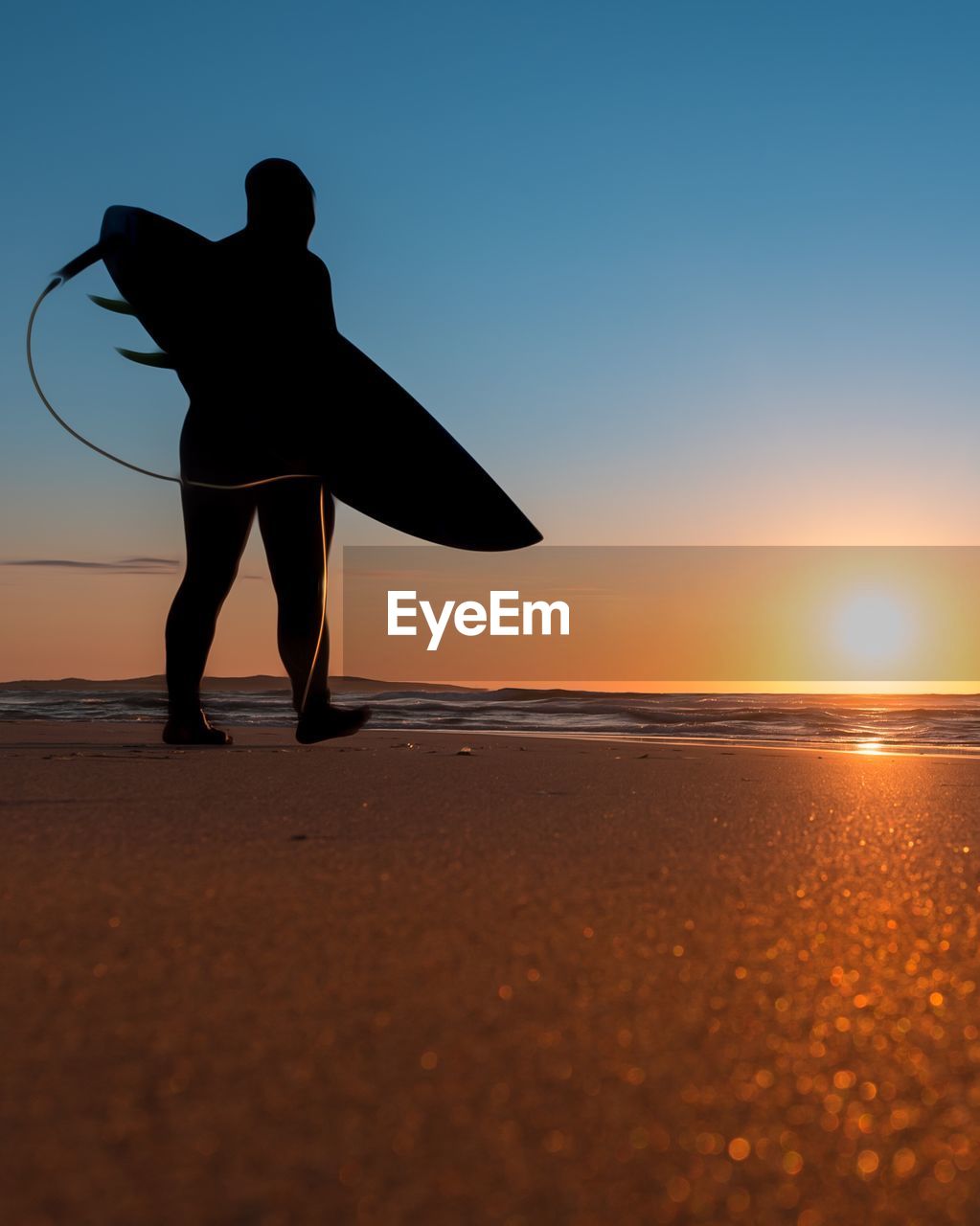 Silhouette man holding surfboard at beach against sky during sunset