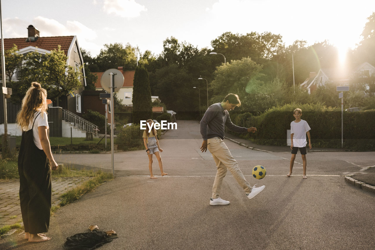 Father playing with soccer ball with family on road