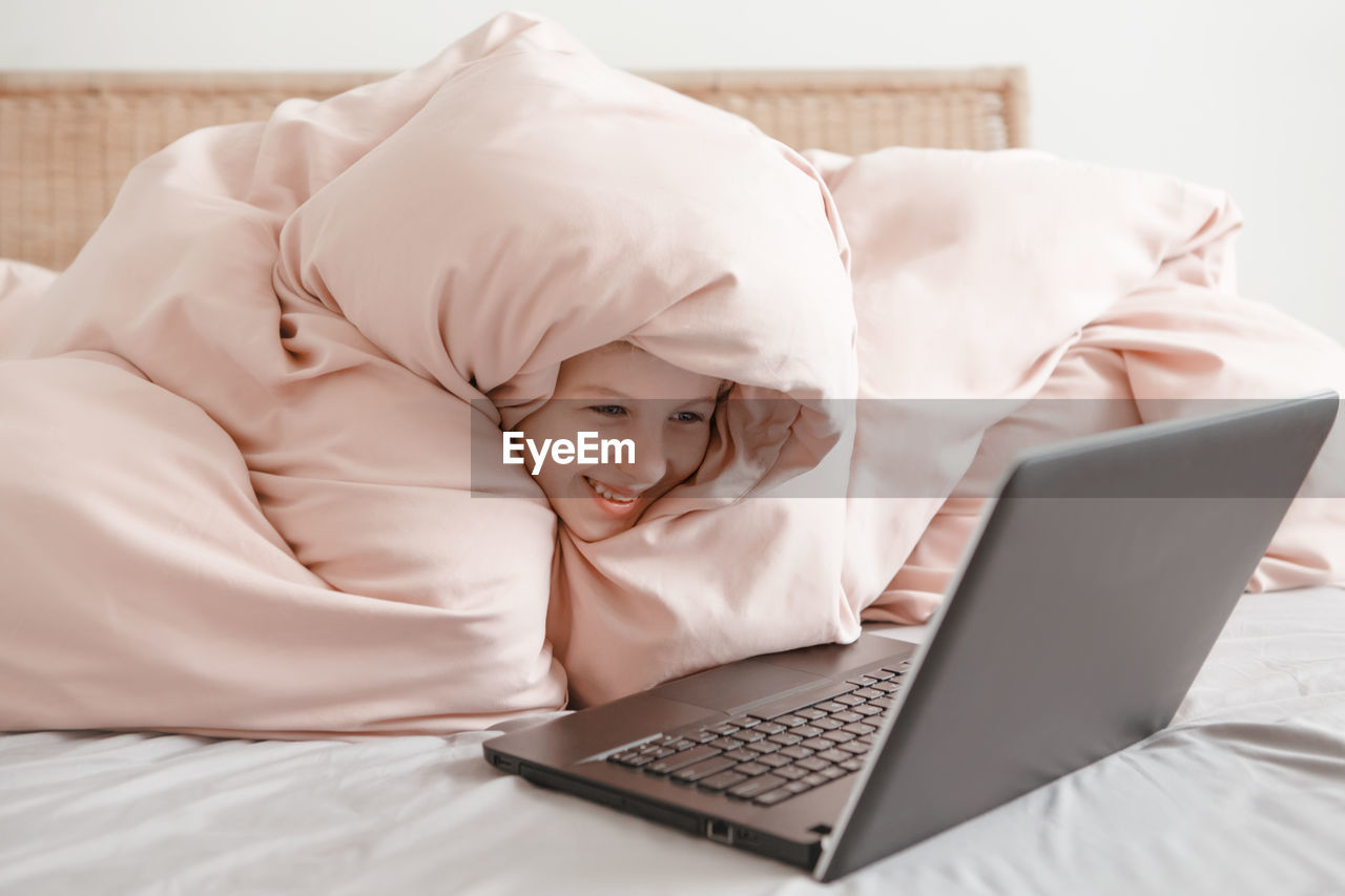 Girl lying in bed under blanket and learning in virtual online school. homeschooling for children