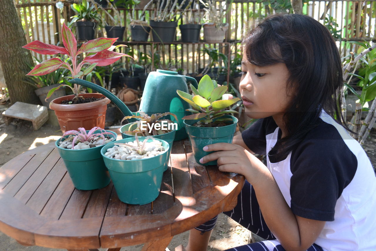 SIDE VIEW OF YOUNG WOMAN SITTING BY POTTED PLANTS