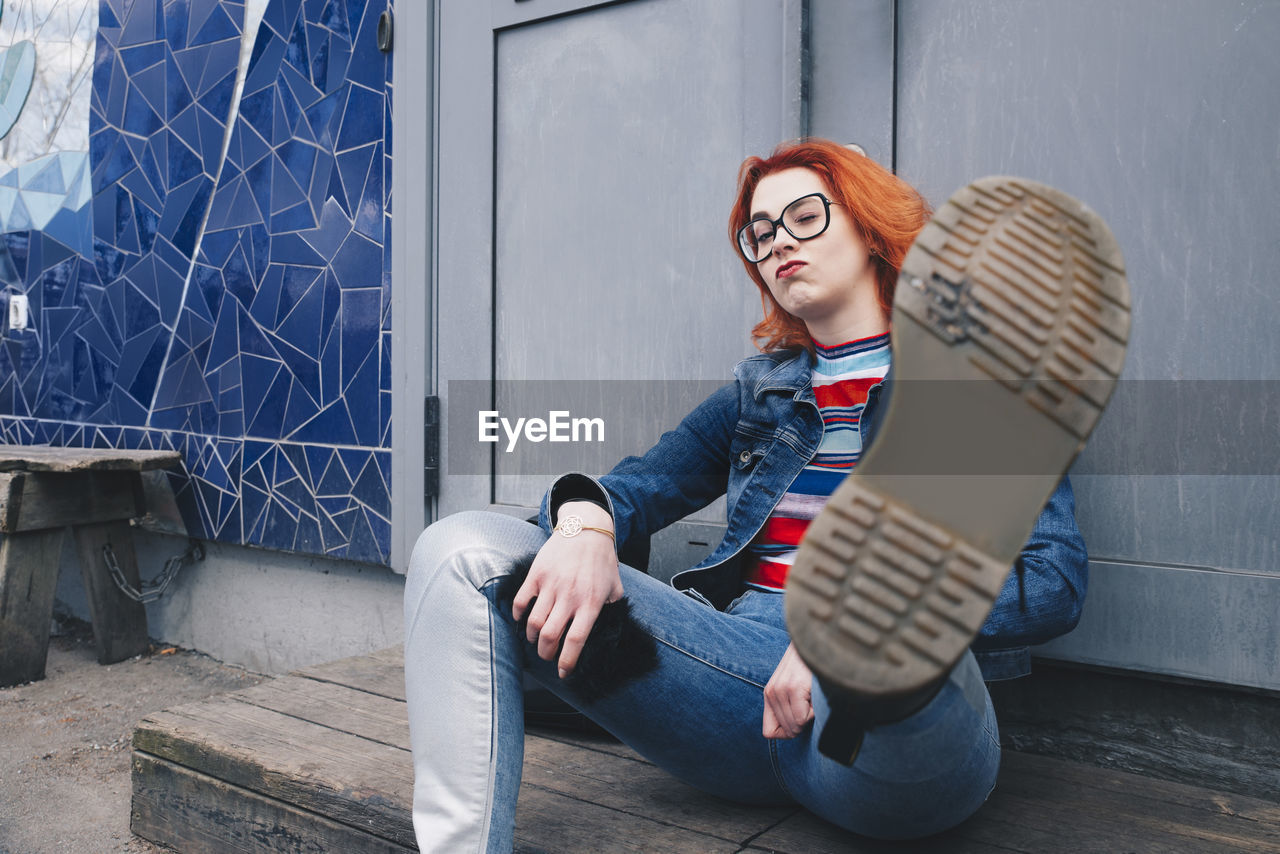 Redhead young woman kicking while sitting against door of building